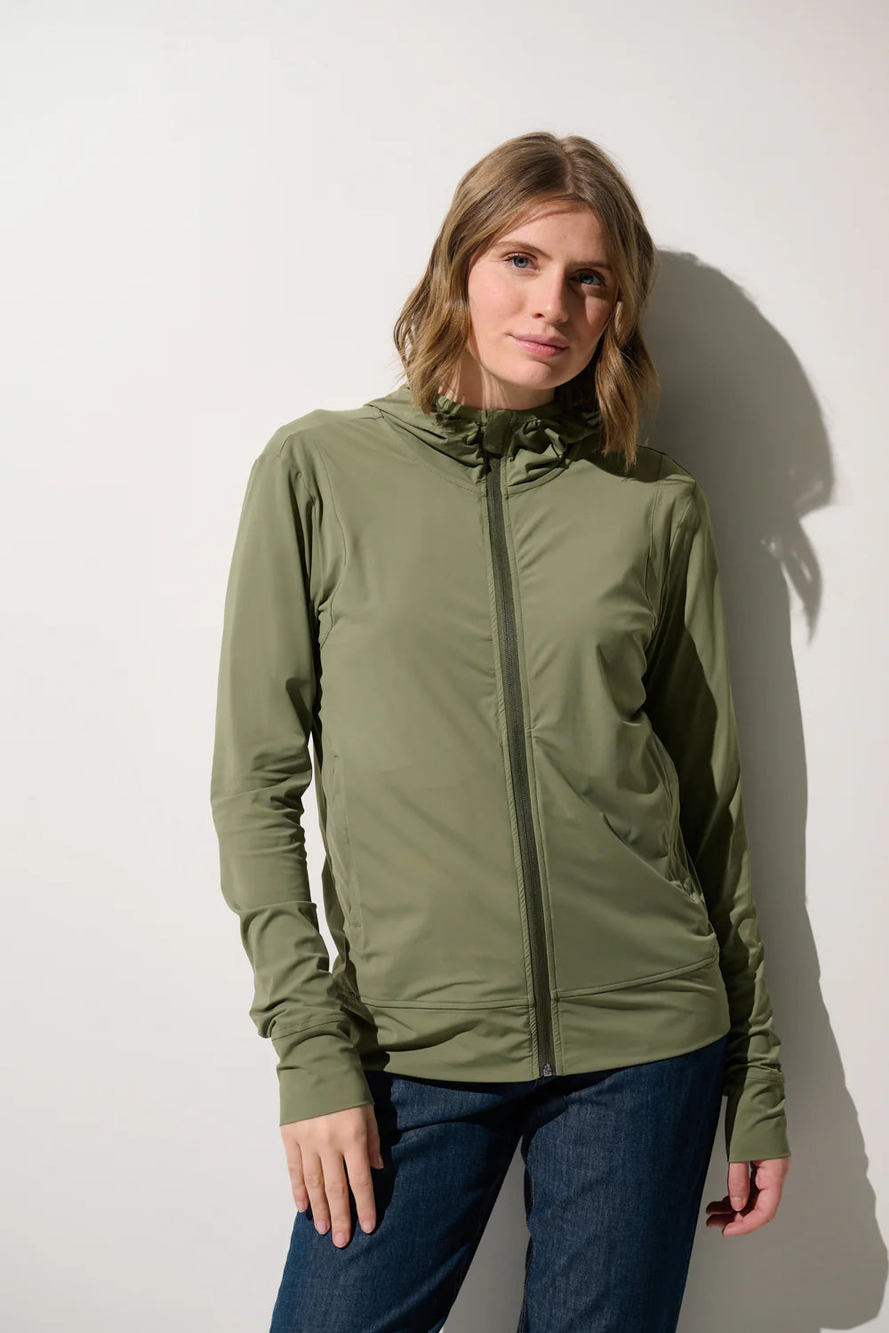 Dame trägt leichte UV Jacke mit Kapuze in einem edel glänzendem Olivgrün. Die Frau posiert vor einem weissen Hintergrund. 